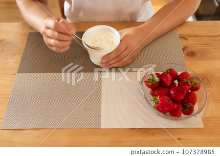 A close-up of a jar of sour cream in a woman's hands and strawberries nearby A close-up of a jar of sour cream in a woman's hands and strawberries nearby 107378985