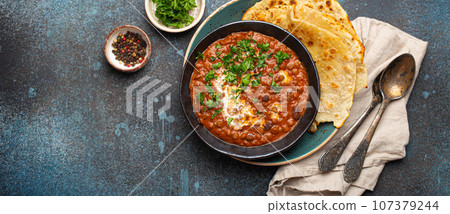 Traditional Indian Punjabi dish Dal makhani with lentils and beans in black bowl served with naan flat bread, fresh cilantro and two spoons on blue concrete rustic table top view. Space for text Traditional Indian Punjabi dish Dal makhani with lentils and beans in black bowl served with naan flat bread, fresh cilantro and two spoons on blue concrete rustic table top view. Space for text 107379244