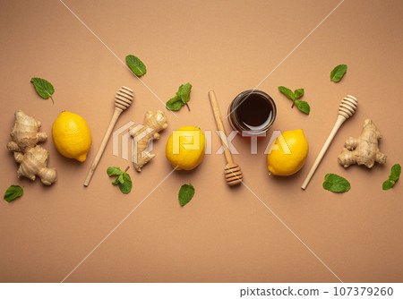 Composition with lemons, mint, ginger, honey in glass jar and honey wooden dippers top view. Food for immunity stimulation and against seasonal flu. Healthy natural remedies to boost immune system Composition with lemons, mint, ginger, honey in glass jar and honey wooden dippers top view. Food for immunity stimulation and against seasonal flu. Healthy natural remedies to boost immune system 107379260