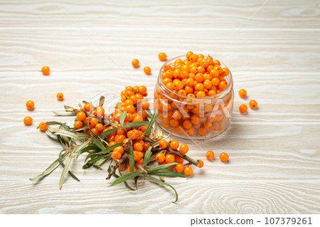 Sea buckthorn ripe berries in glass jar and branches with leaves top view on white wooden rustic background, great for skin, heart, vessels and immune system. 107379261