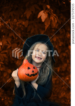 Halloween. The girl laughs and holds a pumpkin in her hands. Halloween. The girl laughs and holds a pumpkin in her hands. 107379535
