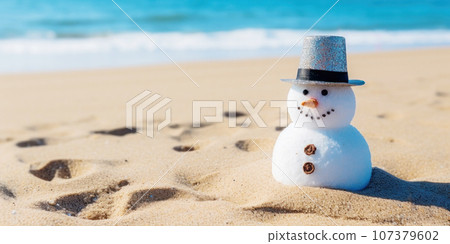 A cute snowman on the beach in bright sunlight, with the sea or ocean in the background. Merry Christmas time, greeting Card. Beach Christmas Vacation without Snow 107379602