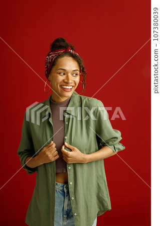 Stylish woman looks away with smile while posing on red studio background Stylish woman looks away with smile while posing on red studio background 107380039
