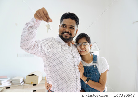 House Ownership. Portrait Of Happy Indian Married Holding Showing Key Standing In New home 107380648