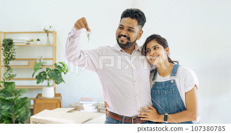 House Ownership. Portrait Of Happy Indian Married Holding Showing Key Standing In New home 107380785
