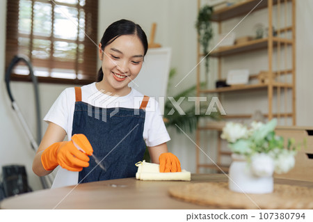 Young woman cleaning using spray and wiping the table with microfiber cloth in living room 107380794