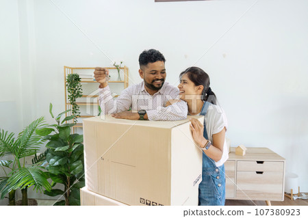 House Ownership. Portrait Of Happy Indian Married Holding Showing Key Standing In New home 107380923