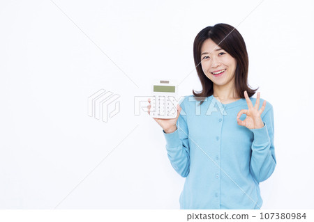 A woman in her 30s holding a calculator and giving an OK sign in front of a white background A woman in her 30s holding a calculator and giving an OK sign in front of a white background 107380984