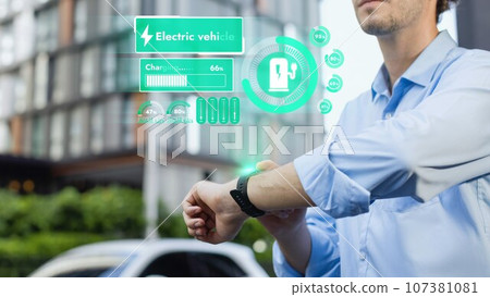 Businessman checking EV car battery status in hologram from smartwactch. Peruse Businessman checking EV car battery status in hologram from smartwactch. Peruse 107381081