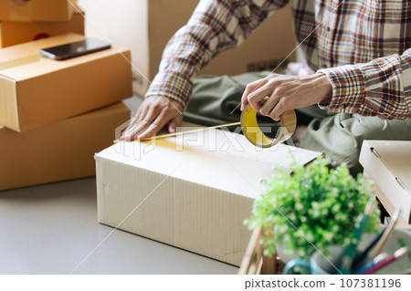 Young man sealing big cardboard box with tape for moving to new home. relocation concept Young man sealing big cardboard box with tape for moving to new home. relocation concept 107381196