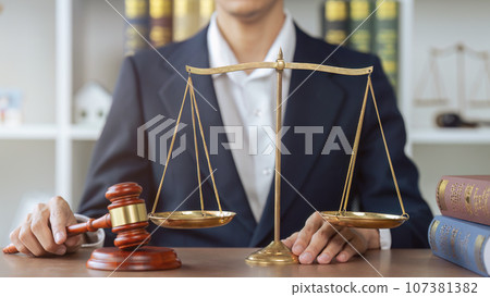 Lawyer man hold a judge's gavel and law scale and books beside in law office 107381382