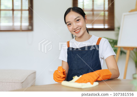 Young woman cleaning using spray and wiping the table with microfiber cloth in living room 107381556