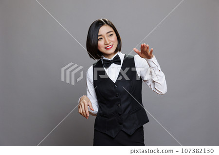 Catering service cheerful smiling asian woman employee dancing. Carefree joyful young waitress wearing uniform making moves with hands while posing in studio on gray background Catering service cheerful smiling asian woman employee dancing. Carefree joyful young waitress wearing uniform making moves with hands while posing in studio on gray background 107382130