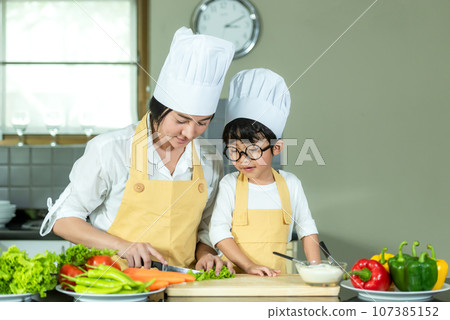 Cooking Family. Chef kid boy and mother making and leaning fresh vegetables salad for healthy eat and education Cooking Family. Chef kid boy and mother making and leaning fresh vegetables salad for healthy eat and education 107385152