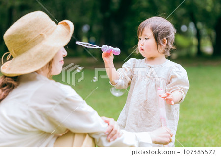 Mom and girl/child playing with soap bubble sticks in the grassland/park 107385572
