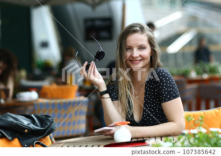 young caucasian woman in polka dot dress, watches and sunglasses close up photo in summer cafe 107385642