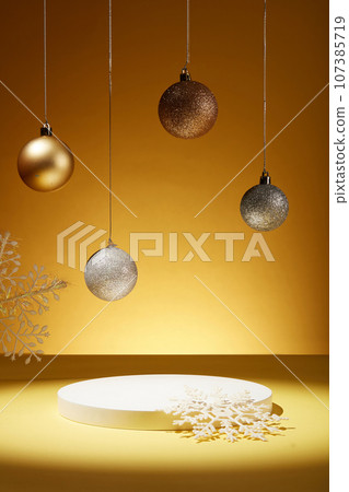 Over the yellow background, several blinking baubles are hanging on. Snow shaped ornaments displayed with an empty podium for product advertising 107385719