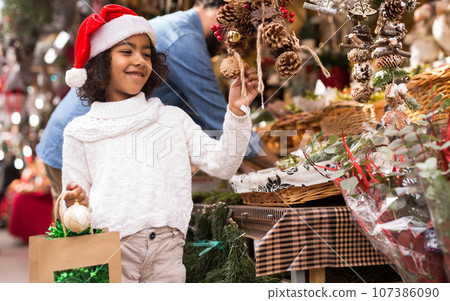 Portrait of joyful small girl in hat choosing Christmas toys Portrait of joyful small girl in hat choosing Christmas toys 107386090