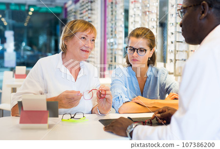 Male and female opticians helping client to choose a spectacles 107386200