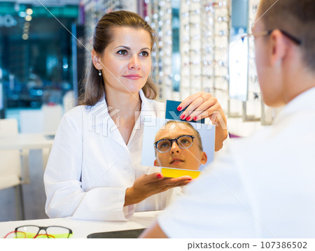 Boy choosing glasses and ophthalmologist holding mirror Boy choosing glasses and ophthalmologist holding mirror 107386502
