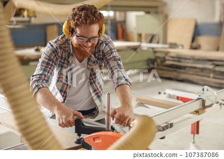 Professional carpenter cutting wooden board at sawmill carpentry manufacturing . Sawing machine Professional carpenter cutting wooden board at sawmill carpentry manufacturing . Sawing machine 107387086