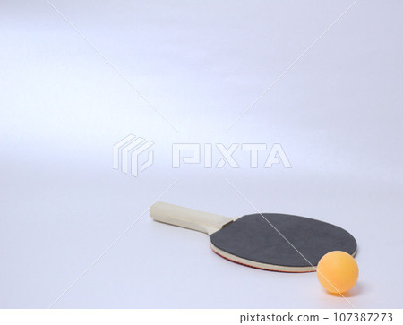 Ping pong ball resting on the black side of the table tennis racket at the bottom right of the screen, white background 107387273