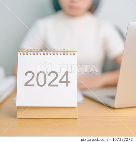 2024 Year Calendar on table with business woman using laptop computer. countdown, Happy New Year, Resolution, Goals, Plan,  Action, Mission and financial Concept 107387278