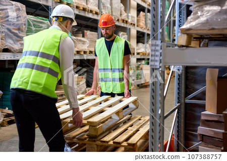 confident warehouse men hold cargo pallet together with co-worker in workplace area confident warehouse men hold cargo pallet together with co-worker in workplace area 107388757