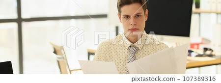 Serious young man holds accounting statistics papers 107389316