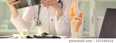 Doctor examines x-ray of patient joint sitting at table Doctor examines x-ray of patient joint sitting at table 107389328
