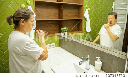 Mature woman brushes teeth in stylish own bathroom at home 107392710