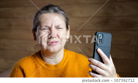 Short-haired woman scrolls social media on black phone at home 107392712
