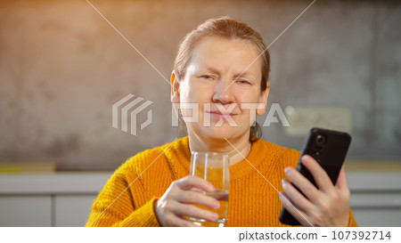Senior woman reading news on phone drinks glass of water 107392714