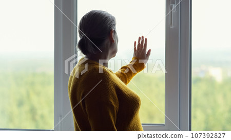 Mature woman missing old time touches window with hand 107392827