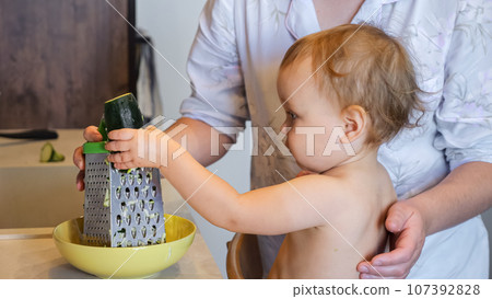 Toddler helps mother to make fresh salad with vegetables 107392828