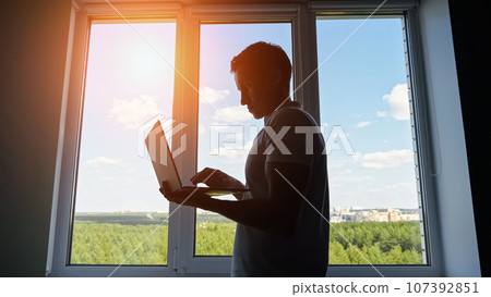 Male office worker walking to window scrolls social media 107392851