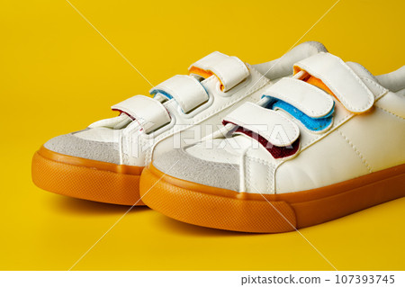 White leather sneakers with fasteners on yellow background White leather sneakers with fasteners on yellow background 107393745