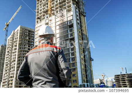 Builder at a construction site. Construction of a high-rise building and a builder looking at the process 107394695