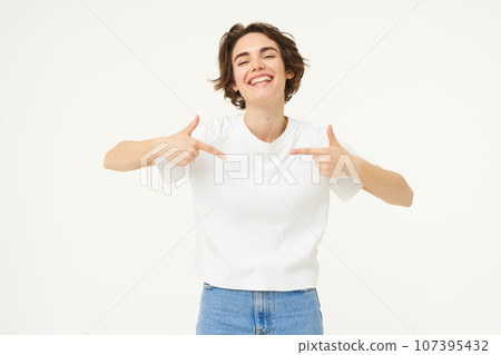 Portrait of smiling, confident girl, pointing at herself with pleased face, standing over white studio background 107395432