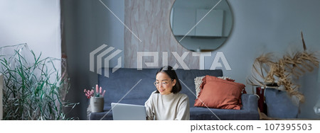 Vertical shot of korean working woman, sitting on floor at home with laptop, studying, using computer on remote, e-learning concept Vertical shot of korean working woman, sitting on floor at home with laptop, studying, using computer on remote, e-learning concept 107395503