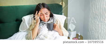 Flu, sickness and people. Young woman feeling sick, having fever and catching col, lying in bed with hot tea, taking drugs from influenza 107395516