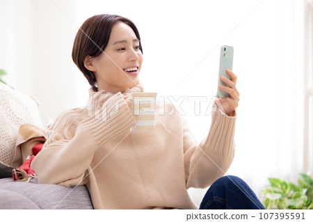 一個女人在客廳裡看著她的智能手機 一個女人在客廳裡看著她的智能手機 107395591