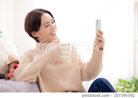 一個女人在客廳裡看著她的智能手機 一個女人在客廳裡看著她的智能手機 107395592