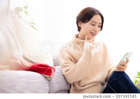 一個女人在客廳裡看著她的智能手機 一個女人在客廳裡看著她的智能手機 107395595