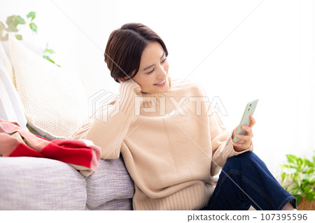 一個女人在客廳裡看著她的智能手機 一個女人在客廳裡看著她的智能手機 107395596