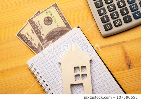 Buy Or Rent concept. Toy house and notepad with calculatoron on wooden background, top view 107396653