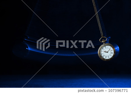 Hypnosis session. Vintage pocket watch with chain swinging over surface on dark background among faded clock faces, magic motion effect Hypnosis session. Vintage pocket watch with chain swinging over surface on dark background among faded clock faces, magic motion effect 107396771