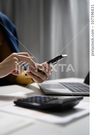 Businesswomen using smartpone with laptop and document on desk in modern office. 107396831