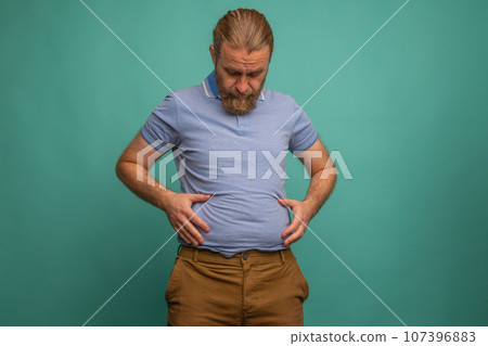 A man with a sad face feels his fat belly on blue background, closeup. Space for text 107396883