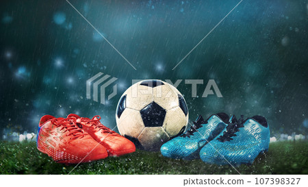 Two pairs of soccer shoes and a ball on the ground as a sign of challenge 107398327